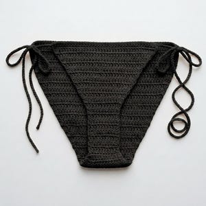 May include: A solid black bikini bottom crafted from crocheted yarn. This swimwear piece features a classic triangular front and back design with adjustable side ties that allow for a customizable fit, showcasing a consistent textured stitch pattern.