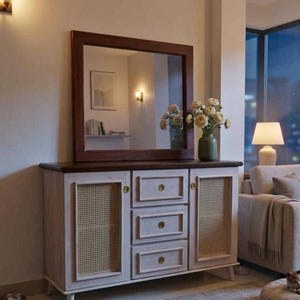May include: A wooden sideboard featuring a white-washed finish, two side cabinets with woven cane panels, and three central drawers with small gold-toned knobs. A large rectangular mirror with a dark brown wooden frame sits on top.