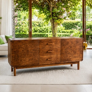 May include: A rectangular wooden sideboard featuring a rich brown wood grain finish, rounded corners, and four tapered legs. The unit includes two side cabinets with solid doors and a central column of three stacked drawers with horizontal handles.