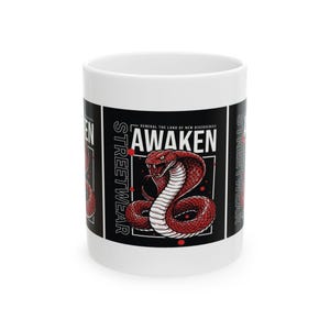 Puede incluir: Una taza de cerámica blanca con un diseño gráfico que muestra una cobra roja en el centro. El texto AWAKEN está impreso sobre la serpiente, con STREETWEAR escrito verticalmente en el lateral. El diseño incluye pequeños puntos rojos sobre fondo negro.