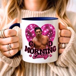 Puede incluir: Una taza de cerámica blanca con asa y borde interior azul oscuro. El frente presenta la imagen de un hombre sin camisa centrado dentro de un gran corazón rosa brillante con forma de bola de discoteca. Debajo, el texto dice "GOD MORNING Emily".