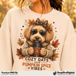 May include: A beige crewneck sweatshirt featuring a graphic of a fluffy brown dog wearing heart-shaped sunglasses and a leopard print bow. The dog holds a coffee cup, surrounded by autumn leaves. Text reads: COZY DAYS and PUMPKIN SPICE VIBES.