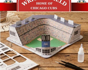Könnte beinhalten: Ein Papiermodellbausatz des Wrigley Field, der Heimat der Chicago Cubs, bestehend aus einer bedruckten Baseballstadion-Struktur, einem Bogen mit Stanzteilen, einer kleinen Klebstoffflasche und einer schwarzen Pinzette zur Montage.