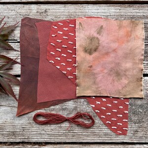 Puede incluir: Un surtido de muestras de tela rojas y rosas con diversas texturas y patrones, incluyendo una pieza con costuras blancas y otra con efecto tie-dye. También hay un ovillo de hilo rojo. Los artículos están dispuestos sobre una superficie de madera envejecida.