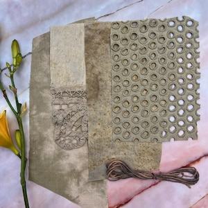 以下が含まれることがあります： ベージュと茶色の色合いの、さまざまなテクスチャードファブリックの見本。レースのデザインと円形の穴あき模様の生地が含まれています。茶色の紐の束も写っています。