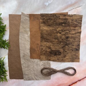 以下が含まれることがあります： 茶色のテクスチャード加工された生地と紙のサンプルがいくつか上から見た写真です。波型の段ボール、しわくちゃの紙、織物、木目模様のテキスタイルが含まれています。紐の束も写っています。