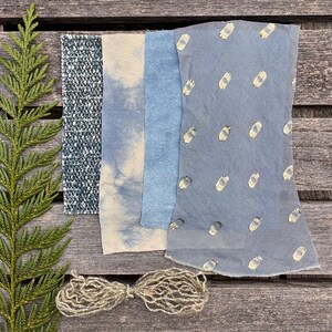 以下が含まれることがあります： さまざまなテクスチャとパターンを持つ青い生地の見本。織り、タイダイ、プリントのデザインが含まれています。自然色の糸の束が下にあります。緑の葉の小枝が左側にあります。