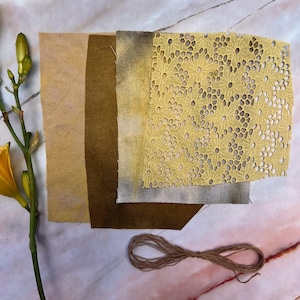 以下が含まれることがあります： 黄色と茶色の色合いの生地見本が並んでいます。花柄のレース生地も含まれています。黄色い花と紐の束も写っています。さまざまな質感と色が、視覚的に魅力的な構成を作り出しています。