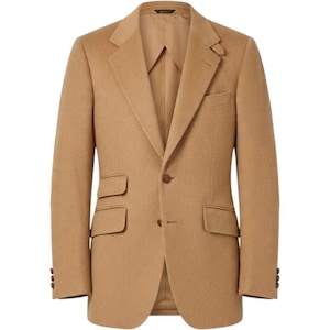 May include: A tan blazer featuring a notched lapel, a single-breasted front with two buttons, and a ticket pocket above the right hip pocket. The jacket includes a chest pocket, long sleeves with three buttons at the cuffs, and a smooth lining.