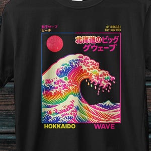 Peut inclure: Un t-shirt noir à manches courtes avec un motif central représentant une vague aux couleurs de l'arc-en-ciel. Le design inclut un soleil rouge, du texte japonais et les mots HOKKAIDO WAVE en jaune et rose, encadrés par un fin liseré.