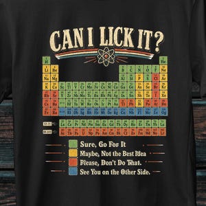 Könnte beinhalten: Ein schwarzes Kurzarm-T-Shirt mit einer Grafik des Periodensystems und dem Text CAN I LICK IT? darüber. Unter der Tabelle erklärt eine Legende die farbcodierten Elemente: Grün für Sure, Go For It, Gelb für Maybe, Not the Best Idea, Rot für Please, Don't Do That und Blau für See You on the Other Side.