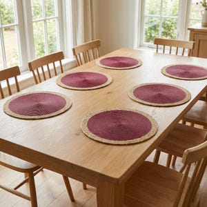 May include: A set of five round placemats arranged on a light-toned wooden dining table. Each placemat features a deep burgundy circular centre with a textured, woven natural tan border. The placemats are flat and circular in shape.
