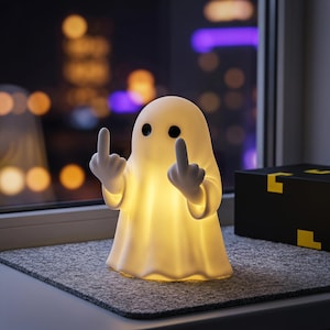 May include: A white, glowing ghost-shaped lamp with two black circular eyes. The ghost figure has two arms raised, with both hands displaying a middle finger gesture. The lamp emits a soft, warm light from within its smooth, rounded body.