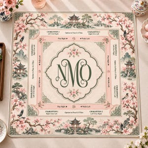 May include: A square Mahjong mat featuring a cream-coloured centre with the dark green monogram NMO, surrounded by a border of pink cherry blossoms, birds, and pagodas. The mat includes printed game instructions like Charleston 1 and 2.