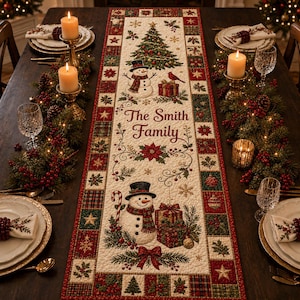 Puede incluir: Un camino de mesa rectangular de tela con un centro color crema que muestra un árbol de Navidad, dos muñecos de nieve, regalos y el texto The Smith Family. El borde presenta un patrón de cuadros rojo y verde con motivos de acebo y estrellas.