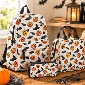 May include: A white backpack, a lunch bag, and a pencil case, all featuring a repeating pattern of orange jack-o'-lanterns, black bats, and witch hats. Each item has black zippers and black trim, showcasing a consistent Halloween-themed design.