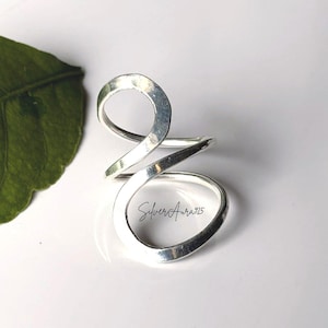 Op de afbeelding: Een ring van gepolijst zilver met een doorlopend, wervelend en open ontwerp dat om de vinger wikkelt. Het metalen oppervlak heeft een gladde, reflecterende afwerking. De tekst SilverAura925 staat in een cursief lettertype op de ring.