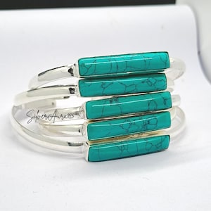 May include: A stack of five silver cuff bracelets, each featuring a rectangular turquoise stone with black veining. The text SilverAura925 is visible on the side of one of the silver bands. The bracelets are arranged in a vertical, overlapping formation.