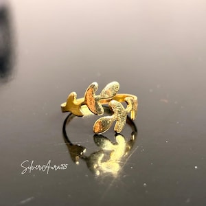 Puede incluir: Un anillo abierto de tono dorado con dos motivos de hojas estilizadas que se encuentran en el centro. La banda es delgada y circular, con las hojas extendiéndose hacia afuera en direcciones opuestas. El texto SilverAura925 es visible abajo.