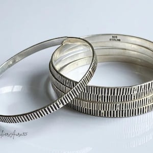 May include: A set of four sterling silver bangles featuring a vertical ribbed texture on the exterior. The interior of the bangles is smooth and stamped with the text 925 STERLING. The text SilverAura925 is visible in the bottom left corner.
