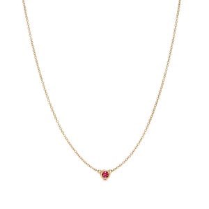 Pode incluir: Um colar de corrente dourada delicada com um único pingente de pedra preciosa rosa, pequeno, redondo e com cravação em bisel, centralizado na parte inferior. A fina corrente de metal conecta-se à base circular que segura a pedra rosa.
