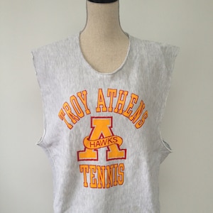 Op de afbeelding: Grijs sleeveless sweatshirt met de tekst "Troy Athens Hawks Tennis" in oranje en rode letters.