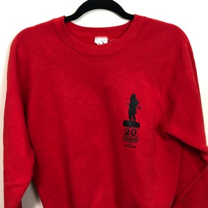 May include: Red sweatshirt with a black silhouette of a soldier holding a rifle. The text "20th Anniversary Battlefields & McCoys" is printed on the front.