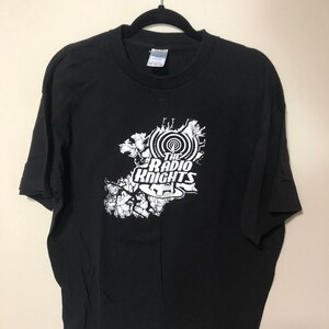 May include: Black t-shirt with a white graphic of a microphone and the text "The Radio Knights".