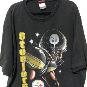 May include: Black t-shirt with a graphic of a Pittsburgh Steelers football player wearing a helmet and jersey. The text "Steelers" is printed vertically on the left side of the shirt.