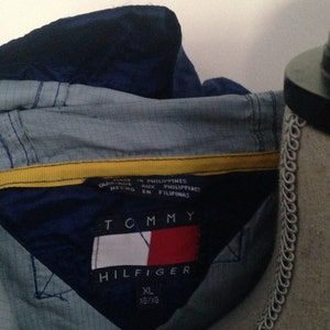 May include: A blue and yellow Tommy Hilfiger jacket with a tag that reads "Made in Philippines, Aux Philippines, En Filipinas". The tag also includes the Tommy Hilfiger logo and the size XL/XG.