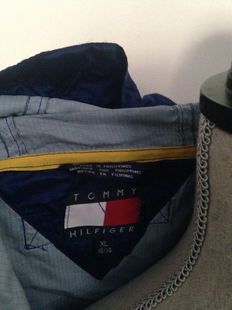 May include: A blue and yellow Tommy Hilfiger jacket with a tag that reads "Made in Philippines, Aux Philippines, En Filipinas". The tag also includes the Tommy Hilfiger logo and the size XL/XG.