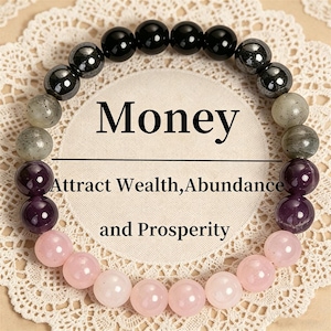 Könnte beinhalten: Ein Perlenarmband mit einer kreisförmigen Anordnung aus polierten, kugelförmigen Perlen in Schwarz, Grau, Dunkelviolett und Hellrosa. In der Mitte steht der Text Money, Attract Wealth, Abundance and Prosperity in einer schwarzen Serifenschrift.