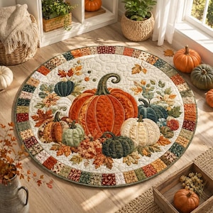 May include: A round quilted rug featuring a central arrangement of pumpkins in shades of orange, cream, and dark green, surrounded by autumn leaves. The border consists of a patchwork pattern of small squares in earthy tones of brown, red, and green.