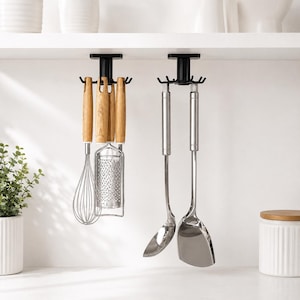 May include: Two black rotating kitchen utensil holders mounted under a shelf. The left holder features wooden-handled tools including a whisk and a grater. The right holder displays stainless steel utensils, specifically a ladle and a spatula.