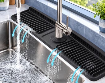 May include: A black silicone faucet splash guard mat with a ribbed, sloped design for water drainage. The rectangular mat features a central cutout for a stainless steel kitchen faucet and sits along the edge of a stainless steel sink.