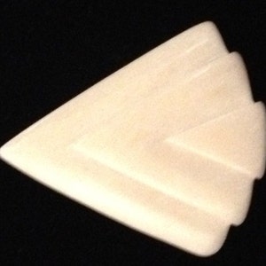 Op de afbeelding: Een witte, cr&egrave;mekleurige, keramische gitaarplectrum met een geometrisch ontwerp. De plectrum is driehoekig met afgeronde randen.