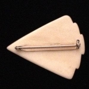 Op de afbeelding: Een witte pijlpuntvormige broche met een zilverkleurige pin aan de achterkant.