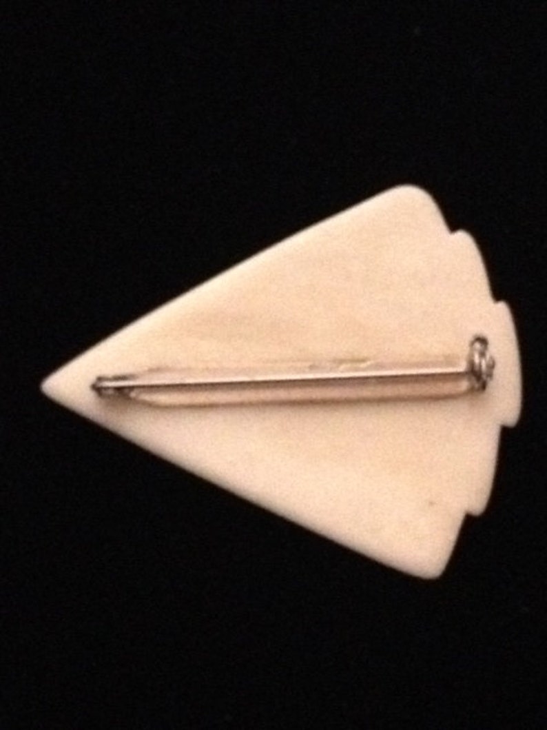 Op de afbeelding: Een witte pijlpuntvormige broche met een zilverkleurige pin aan de achterkant.
