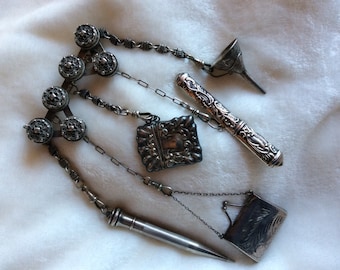 May include: A silver chain with multiple charms, including a small silver funnel, a silver pencil holder, a silver locket, and a small silver purse.