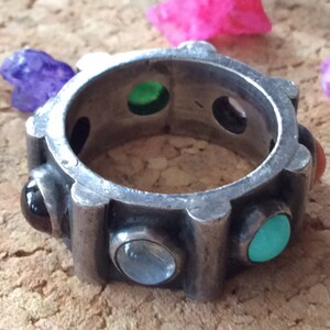 Puede incluir: Un anillo de plata con seis piedras preciosas engastadas en la banda. Las piedras preciosas son negras, verdes, azules, turquesa y rojas.