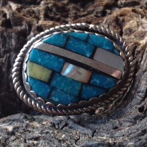 May include: A silver ring with a turquoise and mother-of-pearl inlay. The ring is set in a silver band with a rope-like design.
