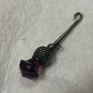 May include: A silver thimble with a purple glass top and a hook on the end.