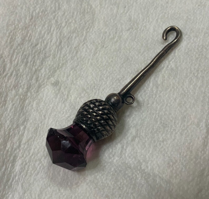 May include: A silver thimble with a purple glass top and a hook on the end.