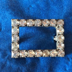 May include: A silver-toned rectangular frame with a border of clear rhinestones. The frame is empty.