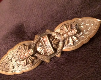May include: A gold-toned brooch with three cross-shaped accents, each adorned with a cluster of faux pearls. The brooch has a detailed, engraved design with floral motifs.