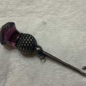 May include: A silver thimble with a purple glass top in the shape of a thistle.