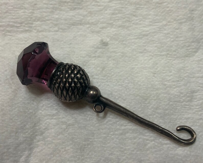 May include: A silver thimble with a purple glass top in the shape of a thistle.