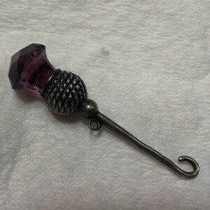 May include: A silver thimble with a purple glass top shaped like a thistle.