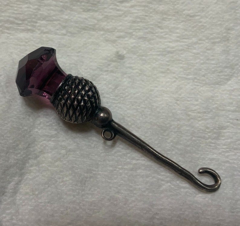 May include: A silver thimble with a purple glass top shaped like a thistle.