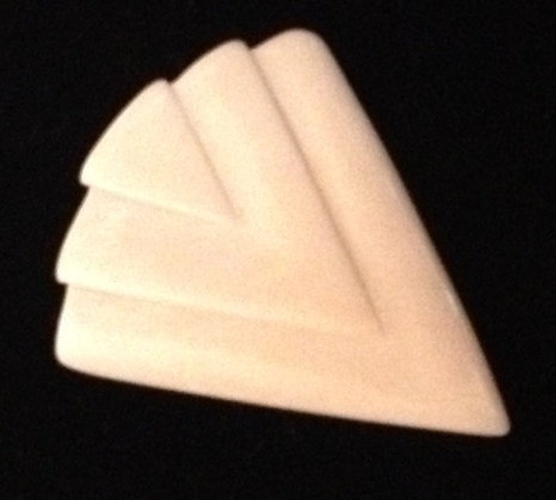 Op de afbeelding: Een witte, driehoekige broche met een geometrisch ontwerp. De broche heeft drie lagen overlappende driehoeken, waardoor een gelaagd effect ontstaat.